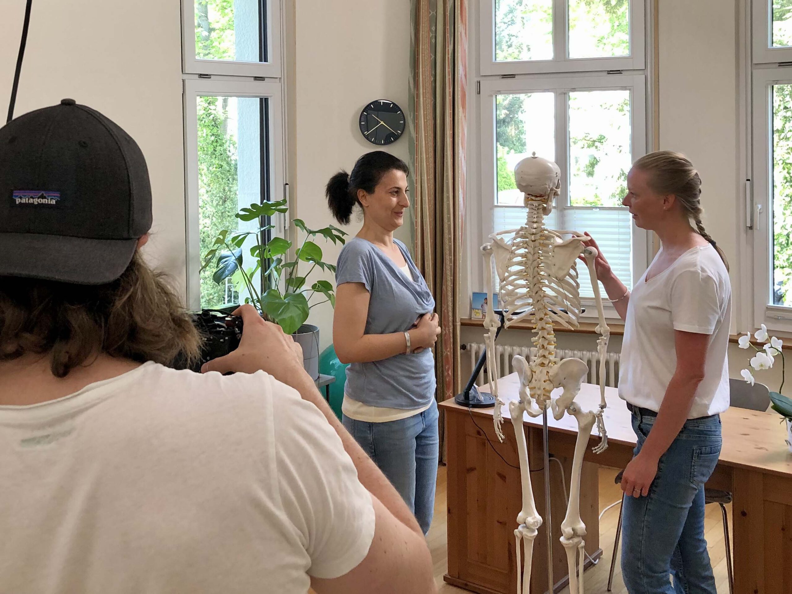 Eine Physiotherapeutin erklärt einer Patientin anhand eines Skeletts die Anatomie des Körpers